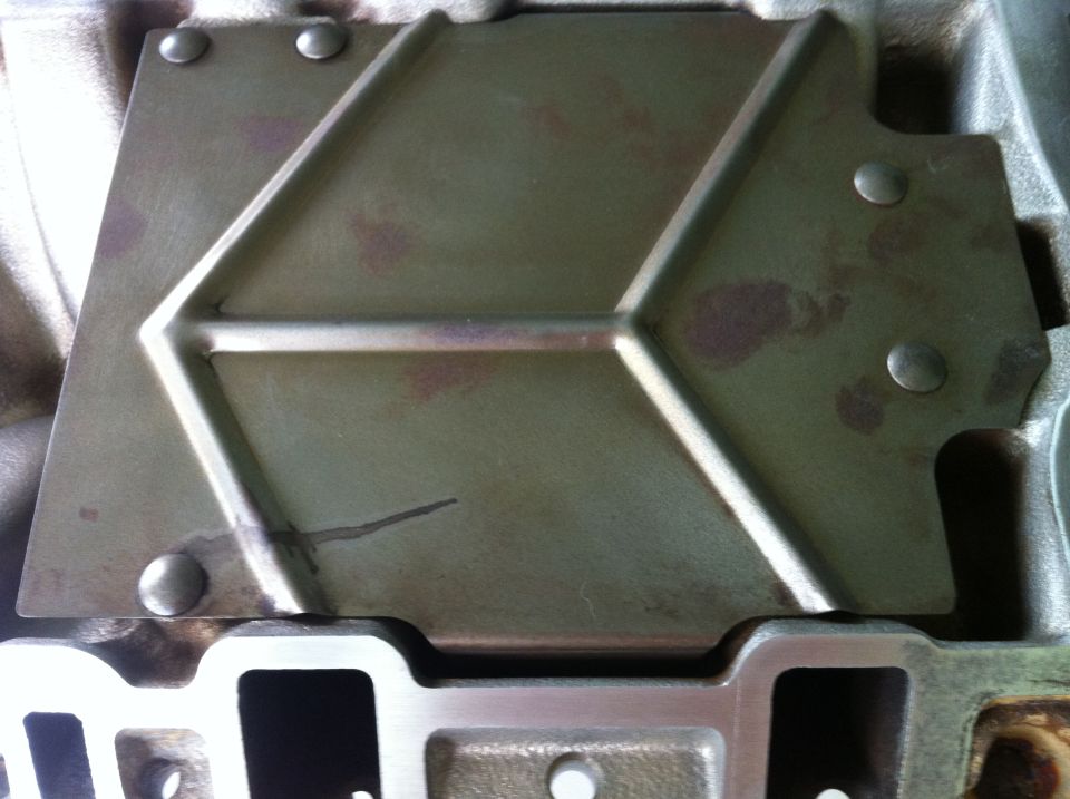 Close-up of an engine intake manifold part with a green metal cover plate