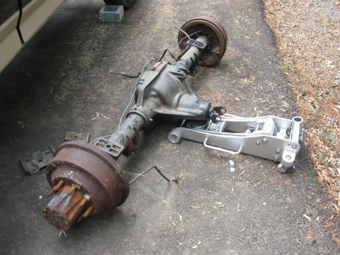 1990 Ford Bronco - A rear axle assembly, likely from a truck or SUV, rests on the ground next to a floor jack.