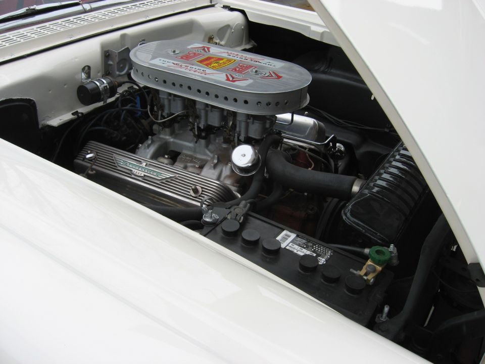 1958 Ford Ranchero engine bay showing V8 engine, dual carburetors, and air cleaner. Battery visible in foreground