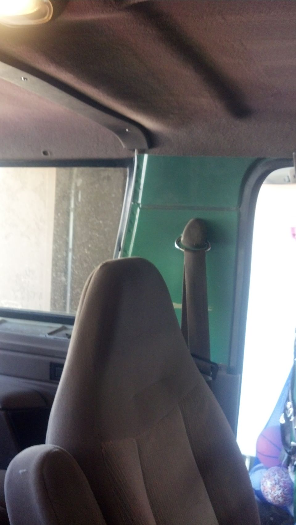 Interior shot of a car showing a tan seat and green paneling. Seatbelt is visible