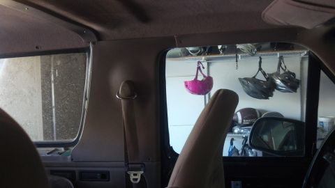 1995 Ford Bronco - View from inside a vehicle shows a pink helmet hanging, with other helmets and sports equipment visible through the window.