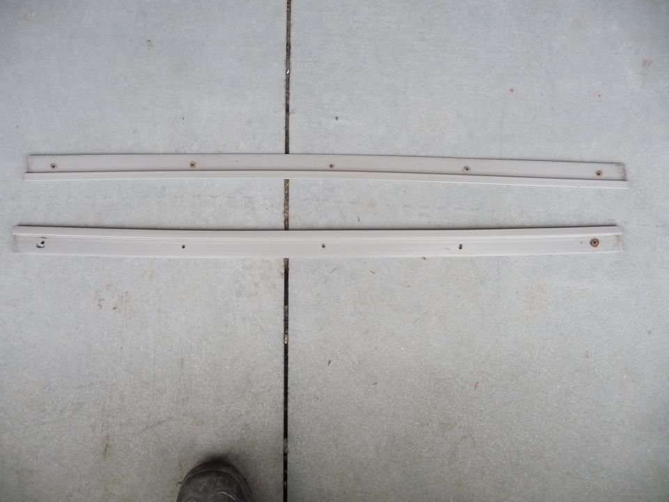 Two beige side skirts with screw holes laid on concrete