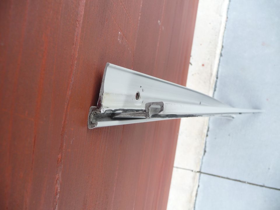 White-painted welded aluminum bracket or rail leaning against rusty surface