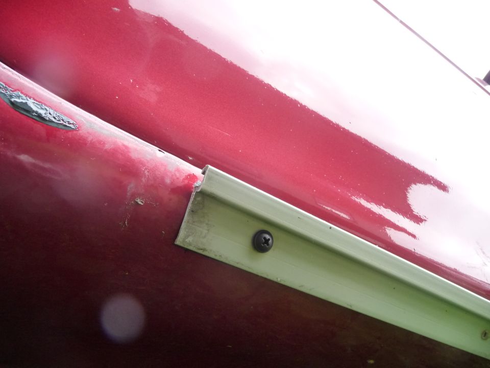 Close-up of a red car's side skirt trim with a screw visible