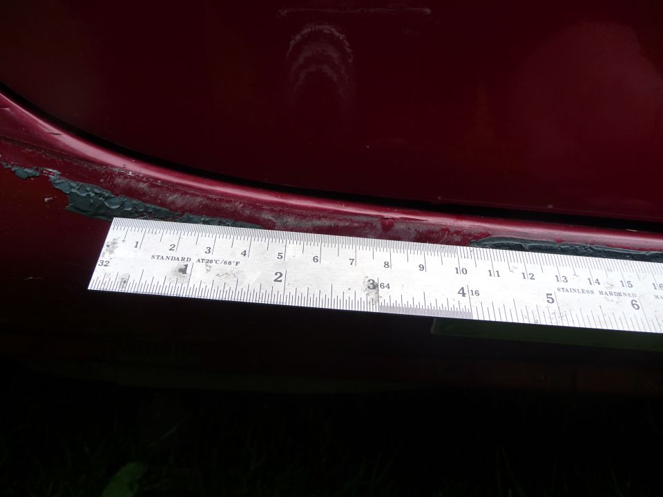 Red car side skirt detail with ruler measuring gap