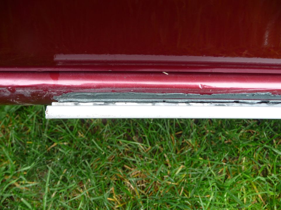close-up of a car's lower door edge with some rust and a white trim piece below