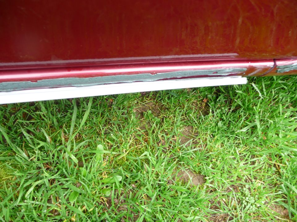 Red car door sill with white trim and grass below