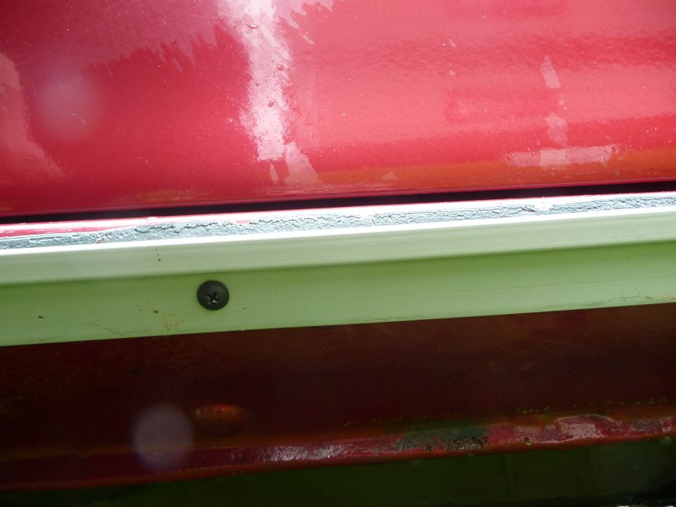 Close-up of a red car's lower body panel showing a white trim piece secured by a screw