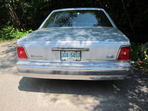 1991 Ford LTD Crown Victoria - The rear of a silver sedan is shown parked outdoors with trees in the background.