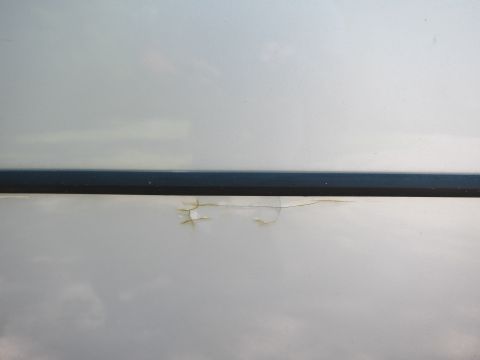 1991 Ford LTD Crown Victoria - Close-up of a silver car door panel shows chipped paint and rust beneath a dark trim piece.