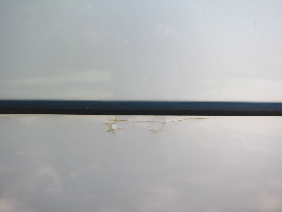 Silver car door panel with a dark trim piece and chipped paint revealing rust