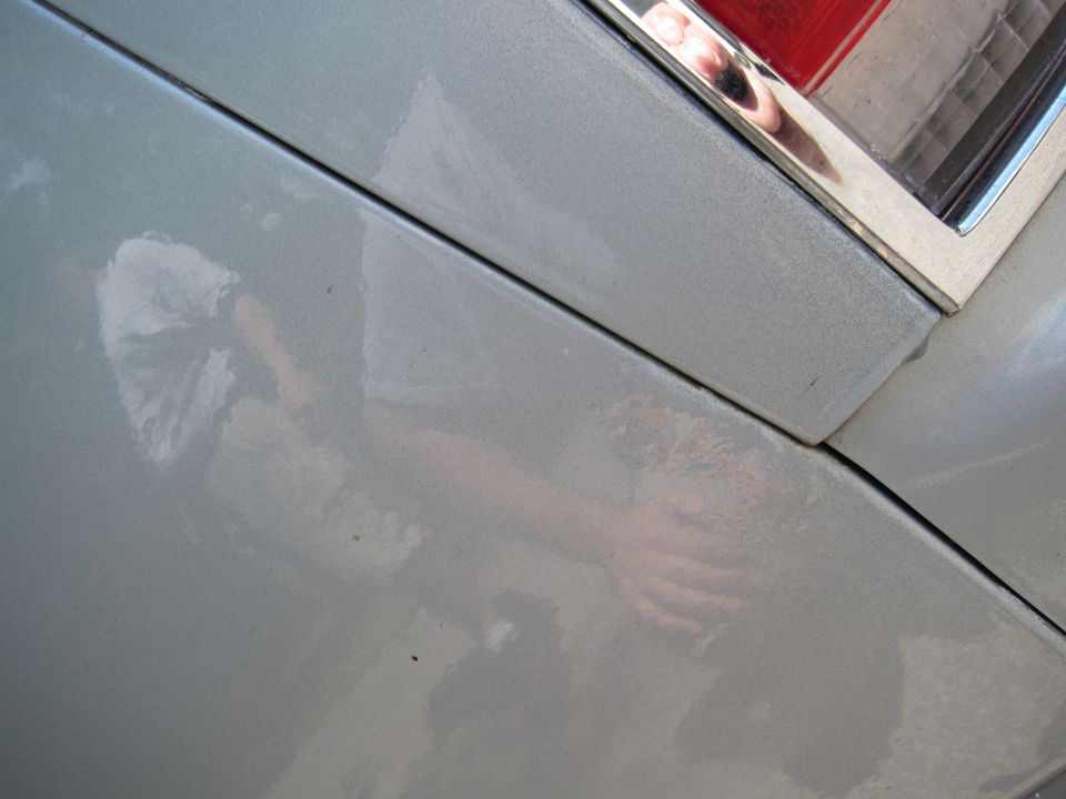 Silver car panel reflecting a person's arm and hand