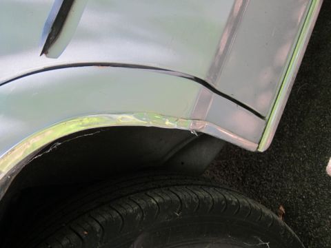1991 Ford LTD Crown Victoria - Dented chrome trim on the rear wheel well of a car.