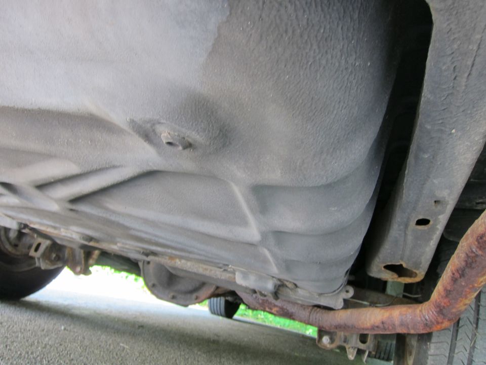 Underside view of a car showing the fuel tank, rusted exhaust pipe, and differential
