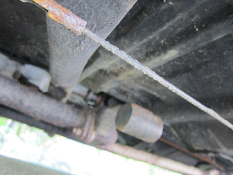 Underbody of a vehicle showing rusted exhaust pipe and cable