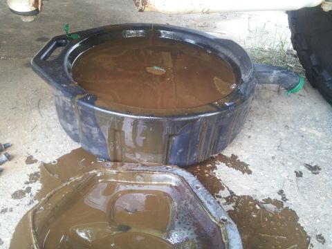 1988 Ford Bronco - Dirty oil is being drained from a vehicle's oil pan into a black drain pan.