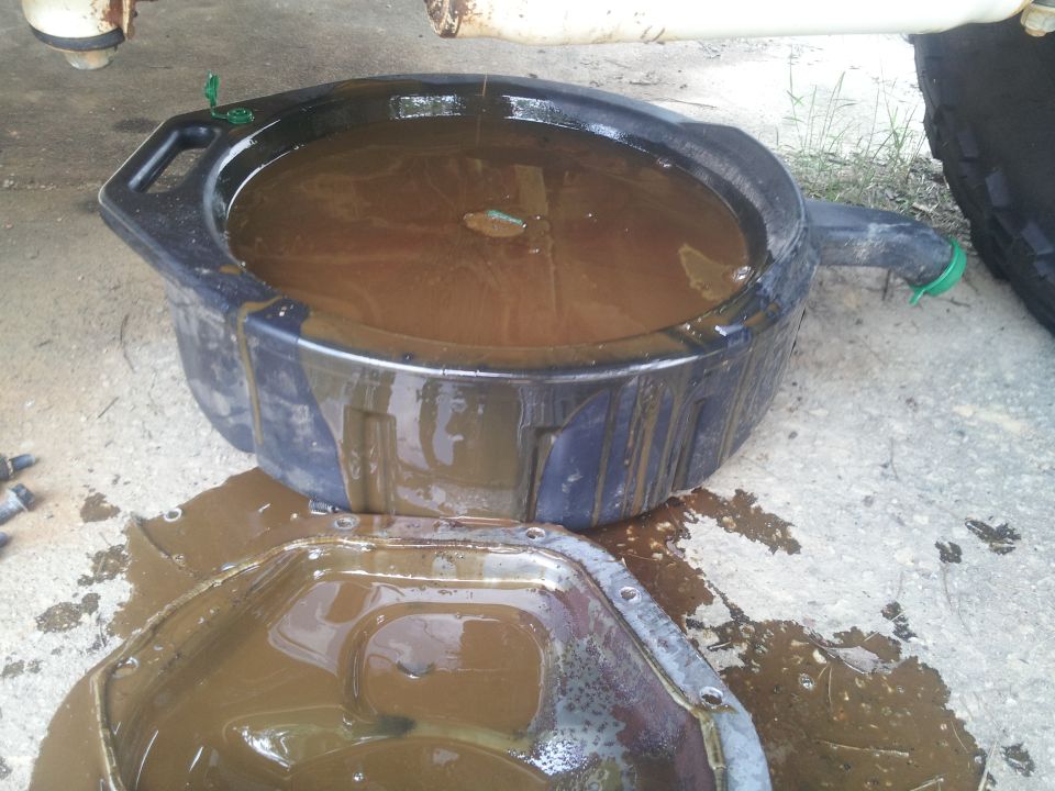 Oil drain pan filled with dirty oil next to an open oil pan
