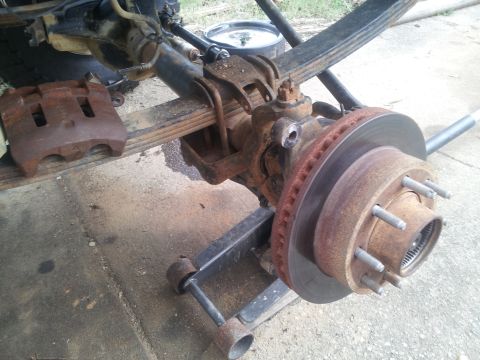 1988 Ford Bronco - Close-up of a heavily rusted brake caliper and rotor assembly, likely undergoing maintenance.