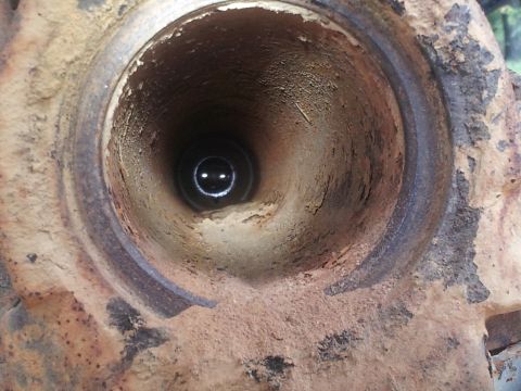 1988 Ford Bronco - The interior of a corroded metal tube is shown, with a dark opening at the far end reflecting light.