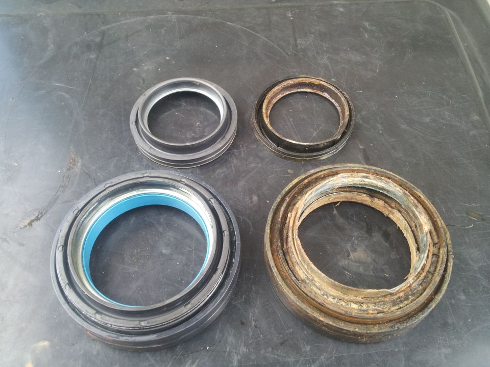 Two new wheel bearing seals and two old, worn-out ones on a dark surface