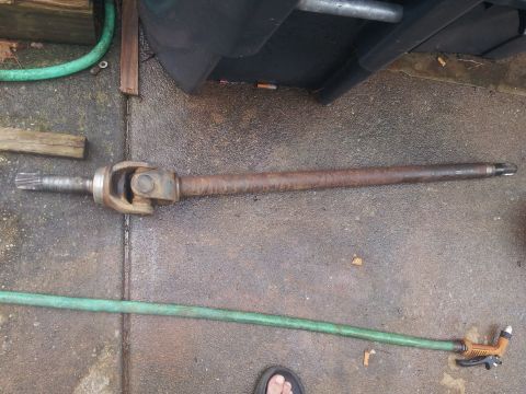 1988 Ford Bronco - A driveshaft with U-joints is shown lying on a concrete surface.