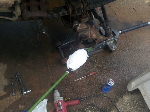 1988 Ford Bronco - Close-up of a vehicle's front axle assembly undergoing repair, with tools and supplies laid out on the ground.