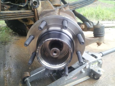 1988 Ford Bronco - Close-up of a vehicle's front wheel hub assembly, showing the splined axle shaft and lug bolts, with a hydraulic jack underneath.