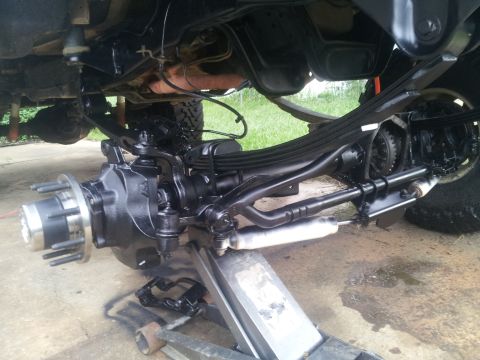 1988 Ford Bronco - The front suspension and drivetrain components of a vehicle are shown, freshly painted black and supported by a jack.