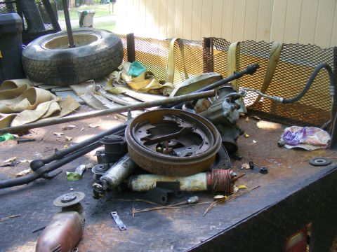 1978 Ford Bronco - A collection of vehicle parts, including a brake drum and steering components, are piled on a trailer.