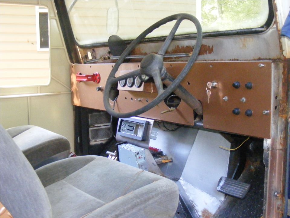 Interior shot of a vehicle with a custom dashboard, aftermarket radio, and two bucket seats. Steering wheel and pedals are visible