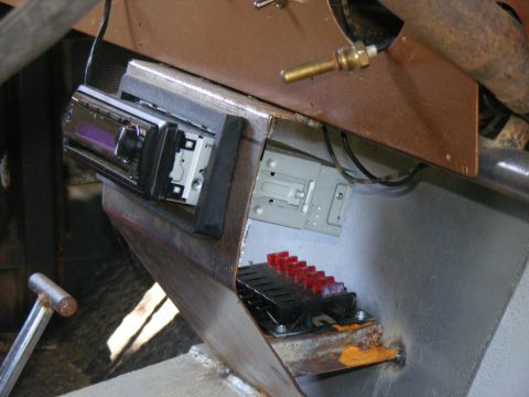 1978 Ford Bronco - Custom metalwork in a vehicle interior holds an aftermarket stereo and a fuse box with red and purple fuses.