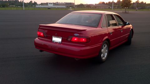 1993 Ford Taurus - A red sedan is parked on an asphalt surface with a stadium in the background.