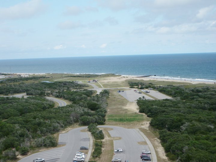 Aerial view of a coastal area with roads, parking lots, trees, and the ocean