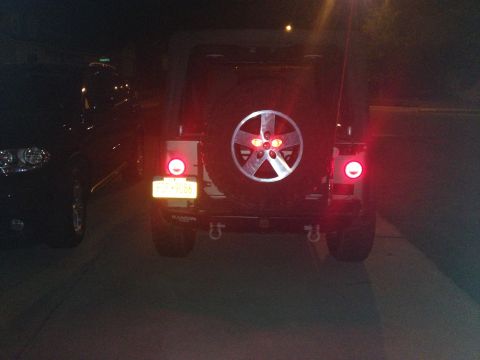 2005 Jeep Wrangler - Rear view of a 2005 Jeep Wrangler, showing the spare tire and taillights. A second vehicle is parked nearby.