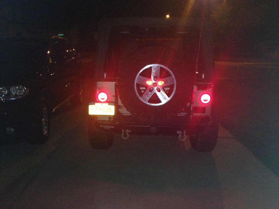 2005 Jeep Wrangler rear view with spare tire and taillights illuminated. Another vehicle is partially visible to the left