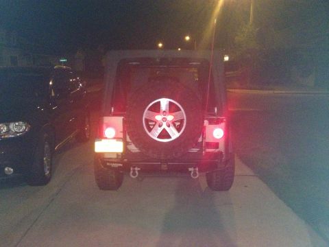 2005 Jeep Wrangler - Rear view of a 2005 Jeep Wrangler, showing its spare tire and taillights. A second vehicle is visible on the left.
