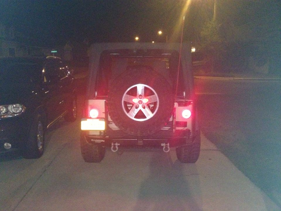 2005 Jeep Wrangler rear with spare tire and tow hooks. Another car is parked to the left