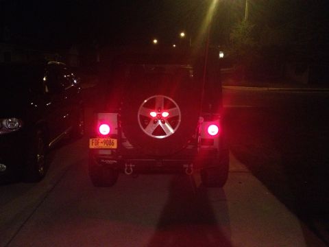 2005 Jeep Wrangler - The rear of a Jeep Wrangler is shown at night, illuminated by its red brake lights and a spare tire mounted on the back.