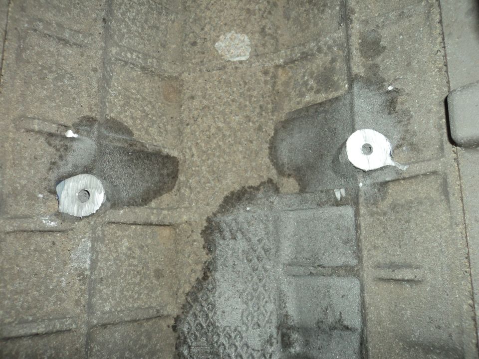 Close-up of a cast metal engine block with two circular metal inserts and some fluid stains
