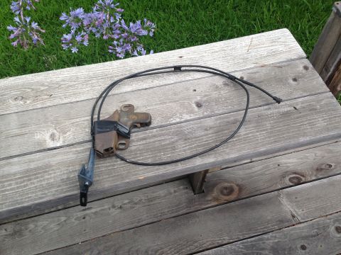 1986 Ford Bronco - A hood latch cable assembly is shown, a black cable and a metal bracket.