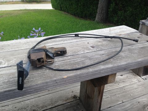 1986 Ford Bronco - Hood latch release lever and cable assembly shown on a wooden surface.