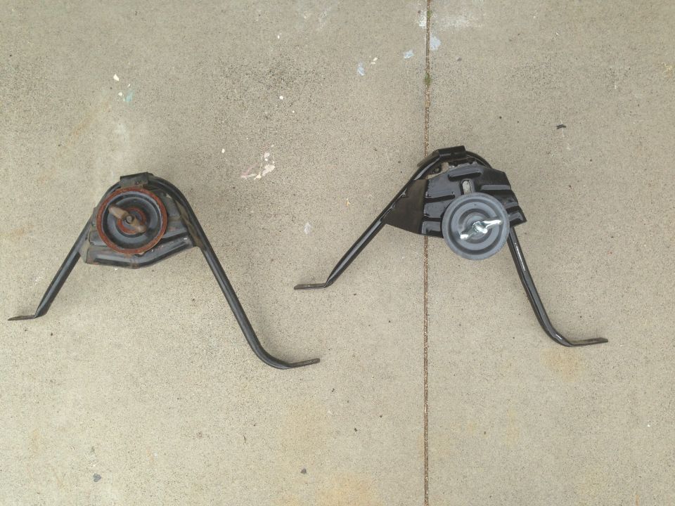 Two black metal engine mounts with rubber dampers on a concrete surface