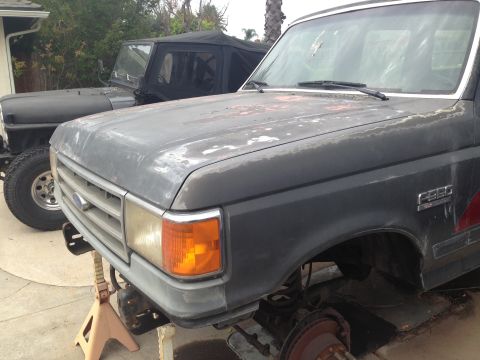 1986 Ford Bronco - The front end of a dark gray 1987 Ford F-250 pickup truck is shown on jack stands, with another vehicle visible behind it.