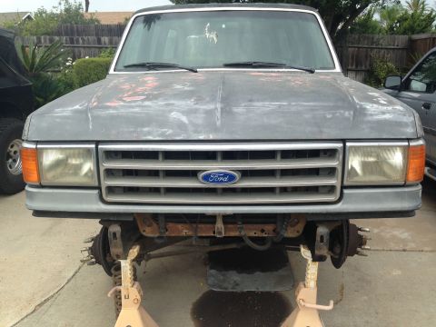 1986 Ford Bronco - Front view of a 1987 Ford Bronco undergoing repairs, with suspension removed and vehicle elevated on jack stands.