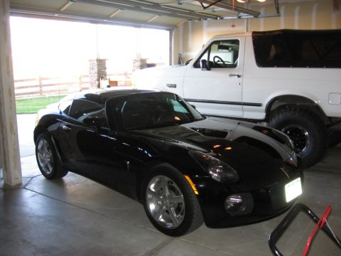 1995 Ford Bronco - Two vehicles, a black sports car and a white SUV, are parked inside a garage.
