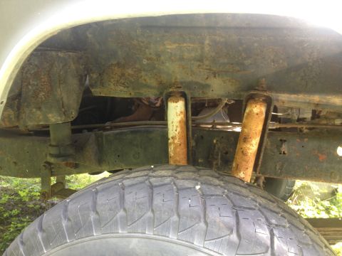 1979 Ford Bronco - The rear suspension components and tire of a vehicle show significant rust.