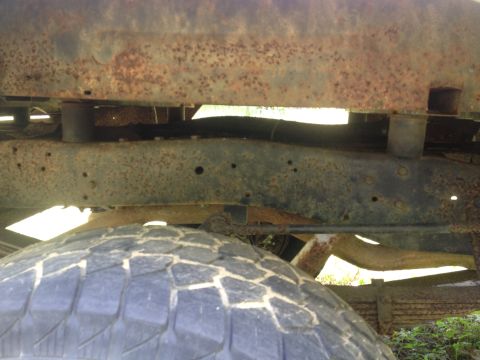 Heavily rusted frame and leaf springs above a tire