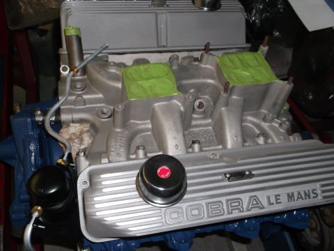 1967 Ford Mustang - A close-up view of a Cobra Le Mans valve cover on an engine, with green tape covering intake ports.