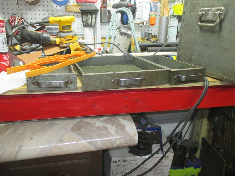 Workbench with a yellow orbital sander, orange plastic tool, and metal drawers containing green liquid