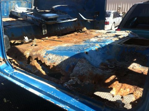 1982 Ford Bronco - The interior of a vehicle shows extensive rust damage, with floor panels and seats removed.
